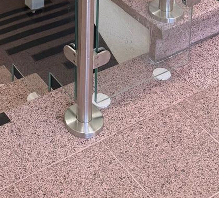 Core drilled stainless steel balustrade post with a cover rose sitting flush on a terrazzo tread